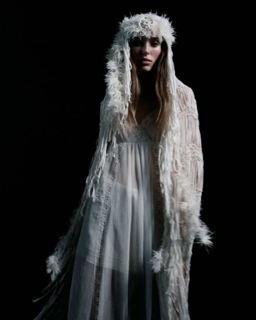 Model wearing a sheer white dress and feathered hood against a dark background for Ann Demeulemeester spring summer 2026