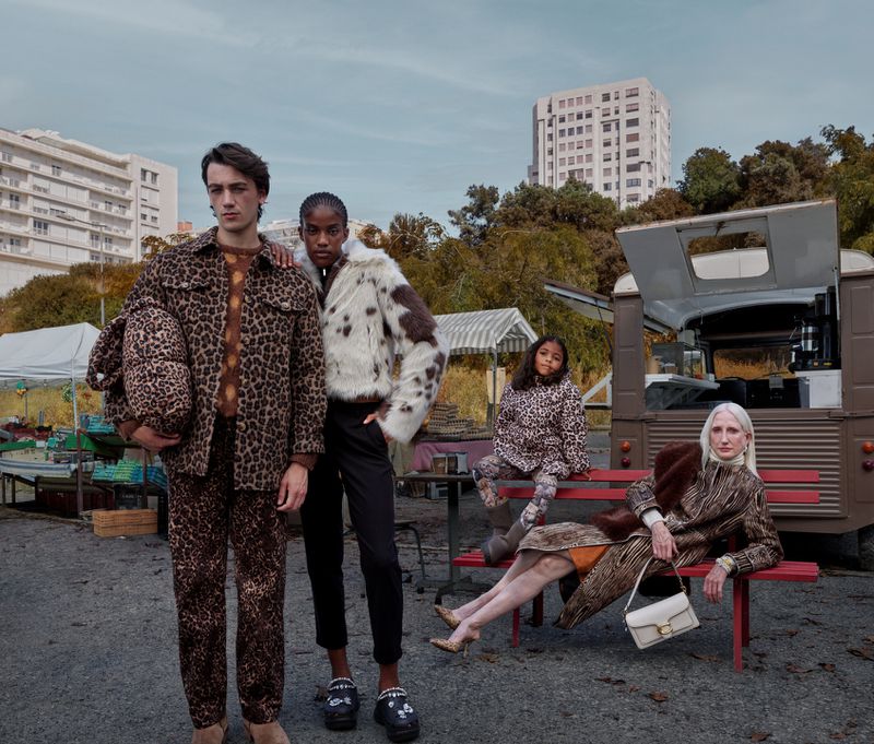 Fashion shoot featuring five models in a gritty urban setting wearing animal print outfits and faux fur coats against a backdrop of a food truck.