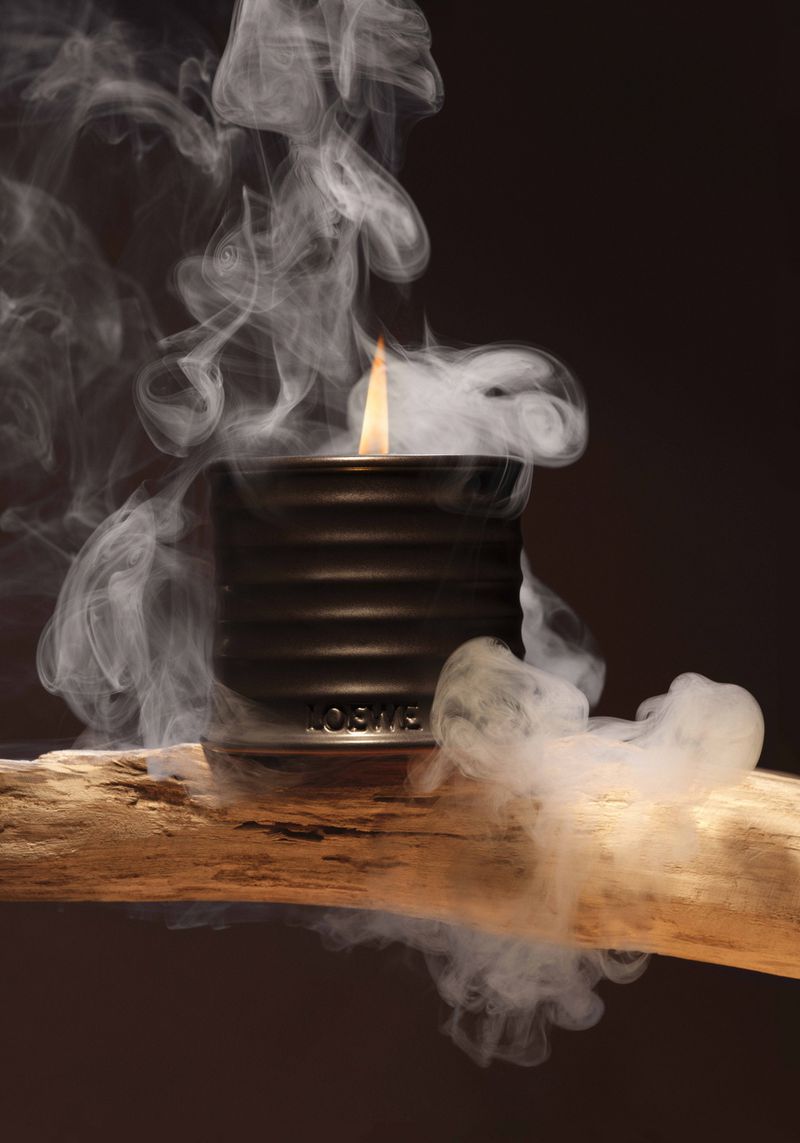 Burning candle on a wooden surface surrounded by smoke against a dark backdrop, creating a moody, atmospheric still life.