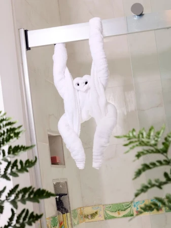 Bathroom towel art of a monkey hanging from a shower door, green fern plant leaves in foreground, creating playful, artistic hotel vibe.