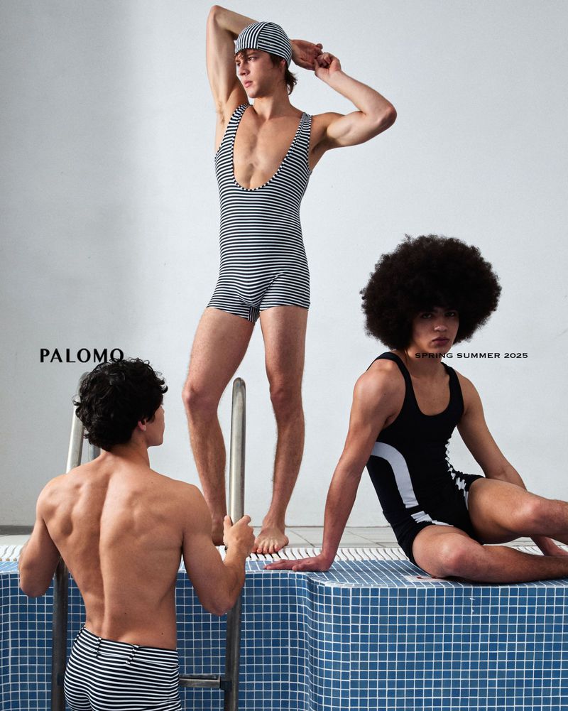 Three men in vintage swimsuits pose next to a tiled swimming pool. One man is climbing a ladder, another is sitting on the edge.