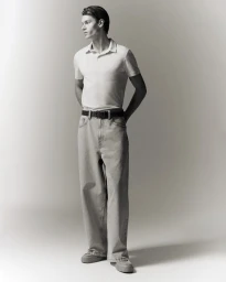 Full-length portrait of a male model wearing a white polo shirt and light grey jeans against a seamless white background.