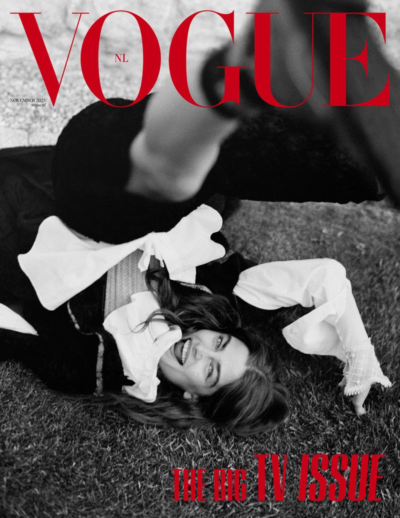 Vogue NL magazine cover featuring a woman in a white top and black jacket lying on grass, with bold red text overlay.