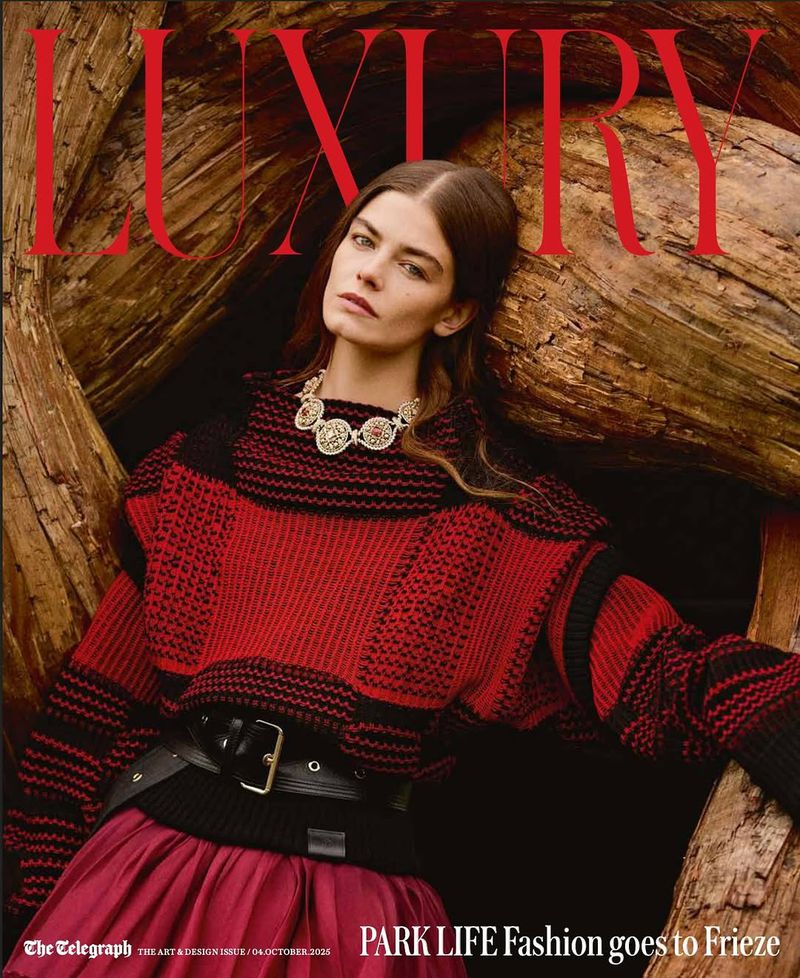 Fashion magazine cover featuring a female model wearing a red and black sweater and jewelry, posing in front of a tree trunk.