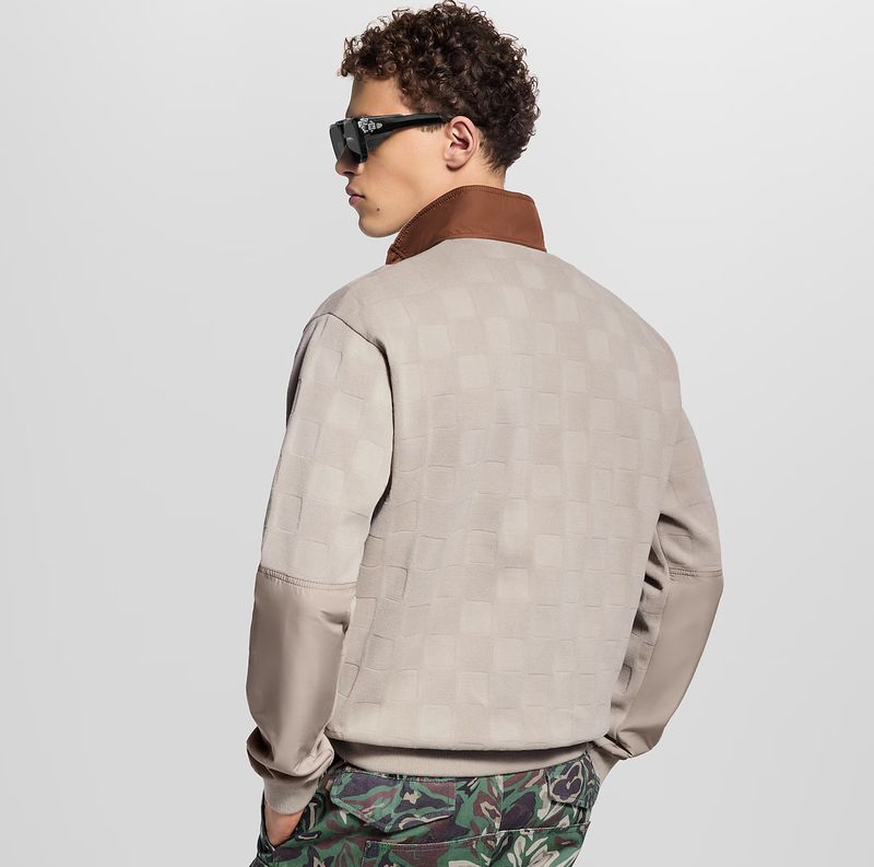 A man with sunglasses, wearing a patterned shirt and camo pants stands against a white backdrop in a fashion or editorial context.