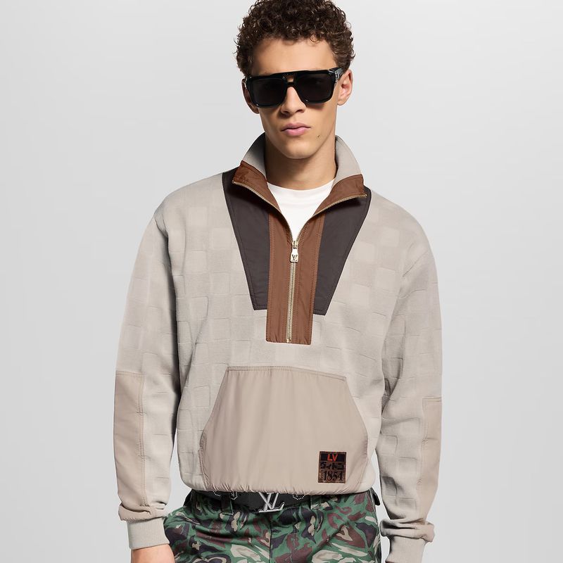 Male fashion model in a patterned sweater with sunglasses, khaki pants, and a belt with a logo in a neutral studio setting.