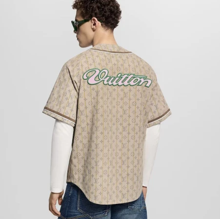 Model wearing a patterned beige jersey over a white long-sleeve shirt with blue jeans against a grey studio background