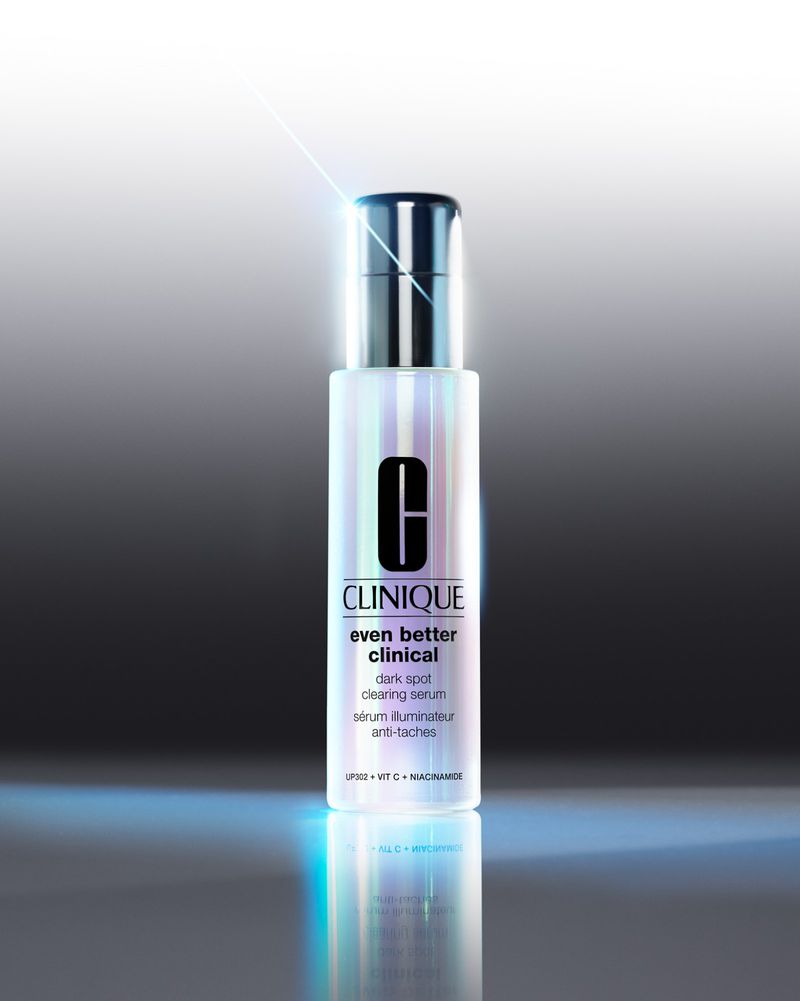 Clinique Even Better Clinical dark spot clearing serum stands against a gradated gray background with a reflective surface.