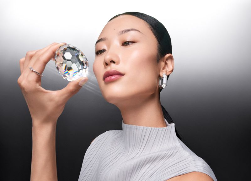 Elegant Asian woman holding a large crystal stone, studio lighting, silver earrings and ring, posing in front of dark gradient backdrop.