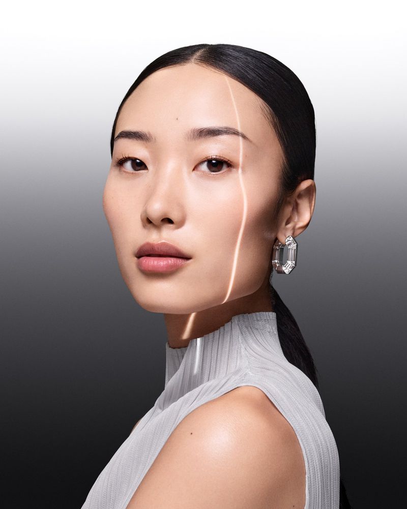 Close-up of an Asian adult woman with elegant crystal earrings, wearing a mock-neck top, against a gradient grey background.