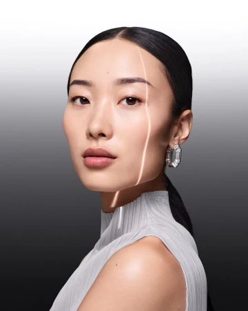Close-up of an Asian adult woman with elegant crystal earrings, wearing a mock-neck top, against a gradient grey background.