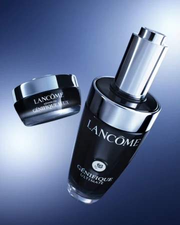Lancome Genifique skincare products featuring a serum bottle and an eye cream against a gradient blue background in a studio shot.
