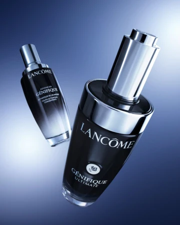 Lancôme Génifique Ultimate anti-aging serum bottles on a blue gradient background. Product still life, beauty, and skincare concept.