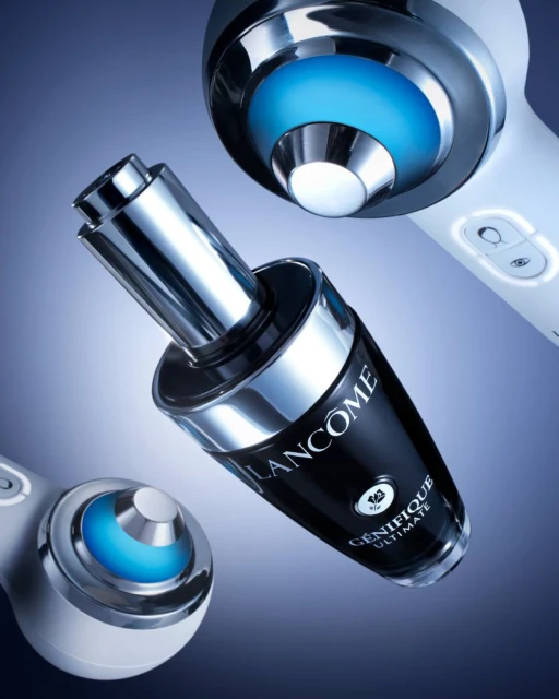 Close-up studio shot of Lancôme Génifique Ultimate serum bottle with chrome accents, next to two skin rejuvenation devices with blue lights.