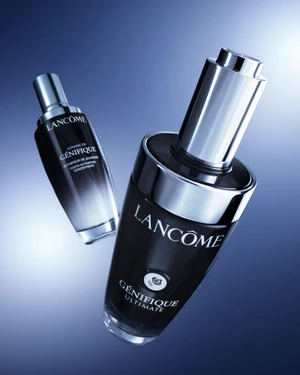 Two Lancome Genifique skincare serum bottles displayed at an angle against a blue gradient background with lighting accents.