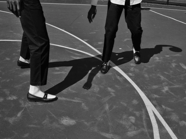 Two adult males in black and white on an outdoor basketball court. The men are wearing dress shoes and stylish pants.