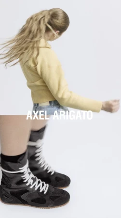 Fashion shot of a woman with blonde hair wearing a yellow jacket and jeans, paired with high-top black sneakers with white laces.