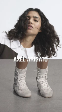 Model with dark curly hair wearing white high-top sneakers and a collared top for Axel Arigato A/W25 campaign.