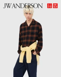 Model with blonde hair wearing a brown plaid shirt and dark trousers against a white background