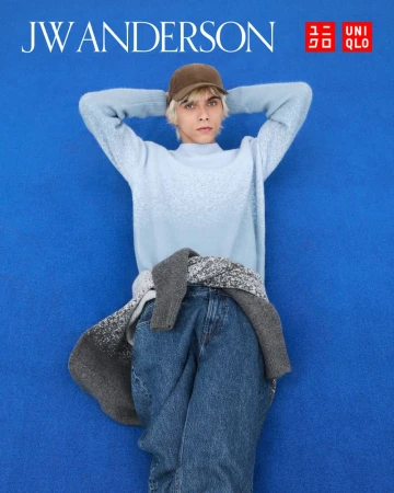 Model wearing a light blue sweater and baseball cap lying on a vibrant blue background for the Uniqlo x JW Anderson F/W 2025 campaign.