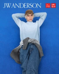 Model wearing a light blue sweater and baseball cap lying on a vibrant blue background for the Uniqlo x JW Anderson F/W 2025 campaign.