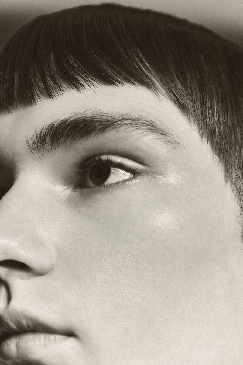 Close-up portrait of a person with dark blunt-cut bangs and natural skin texture shot for Schon Magazine