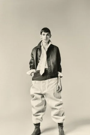 Model in leather jacket and oversized trousers standing against a pale grey seamless background