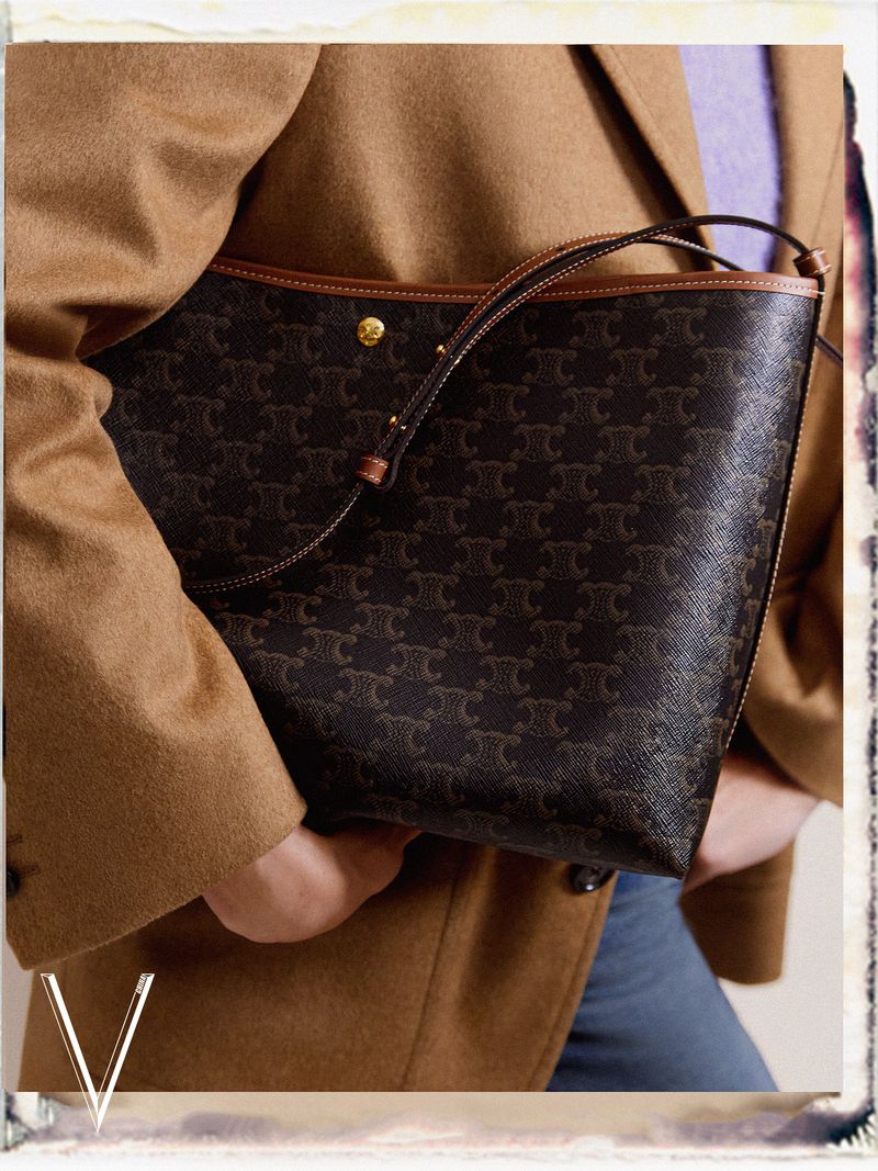 Woman holding a brown Celine handbag with a repeating pattern. The handbag has a brown handle and gold button detail.