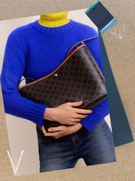 Model holding a monogram handbag wearing a blue sweater and yellow turtleneck over jeans
