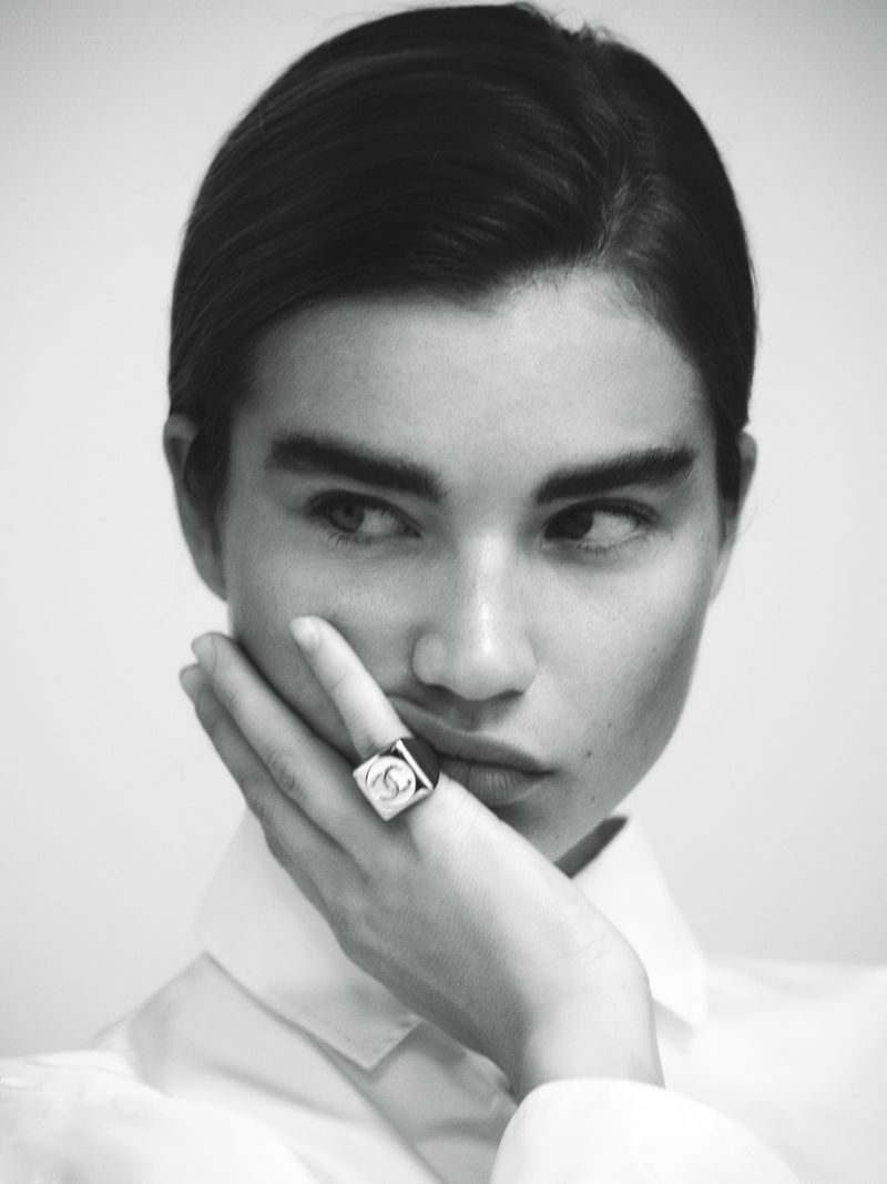 Close-up black and white portrait of model Meghan Roche wearing a statement ring and white collared shirt against a seamless background.