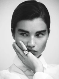 Close-up black and white portrait of model Meghan Roche wearing a statement ring and white collared shirt against a seamless background.