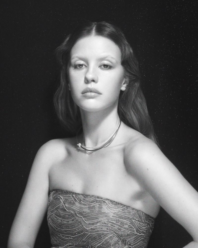 Portrait of a young woman with long hair and a strapless dress, set against a dark backdrop in a studio environment.
