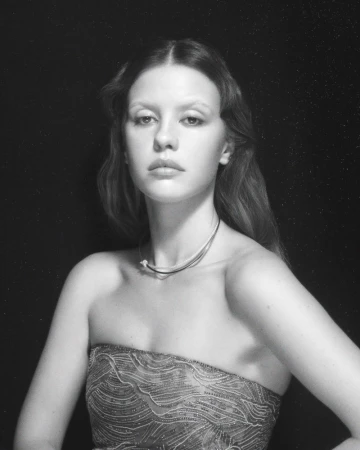Portrait of a young woman with long hair and a strapless dress, set against a dark backdrop in a studio environment.