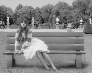 Mia Goth sitting on a park bench wearing a striped top and layered skirt in a monochrome photograph for Vogue Italia