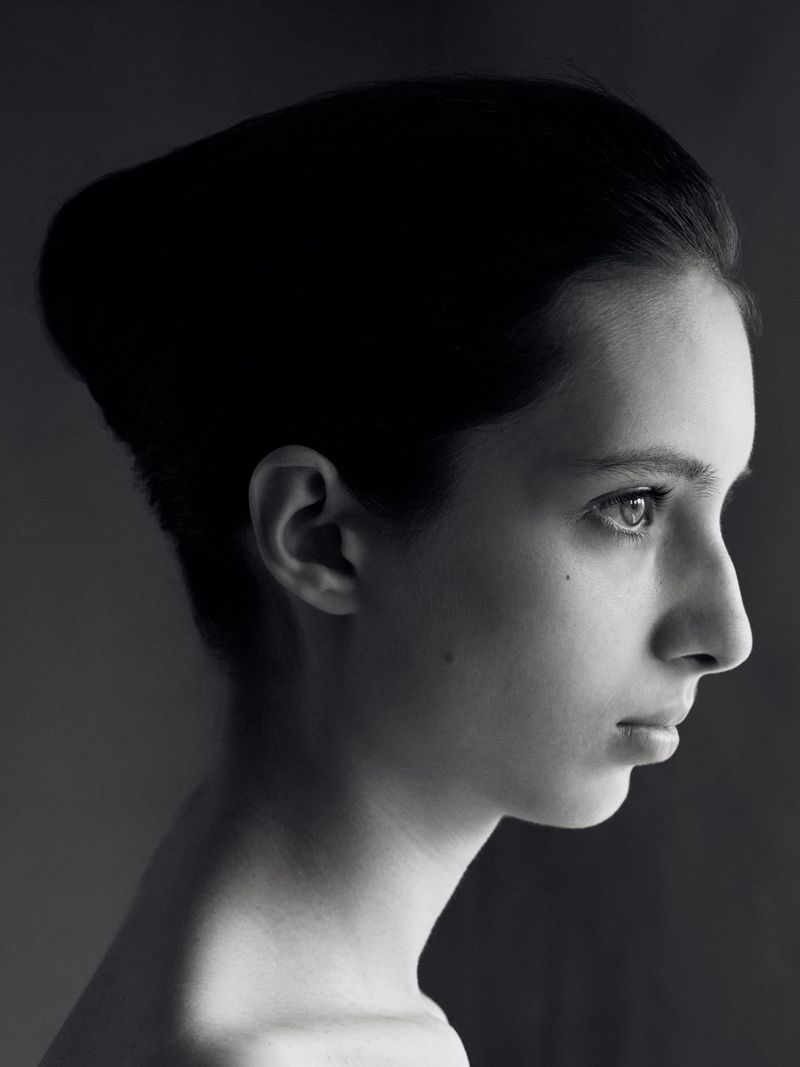 Black and white portrait of a young woman in profile. Her dark hair is neatly styled, and she has fair skin. The background is a soft grey.