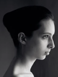 Profile portrait of a woman in monochrome with dark styled hair against a dark background