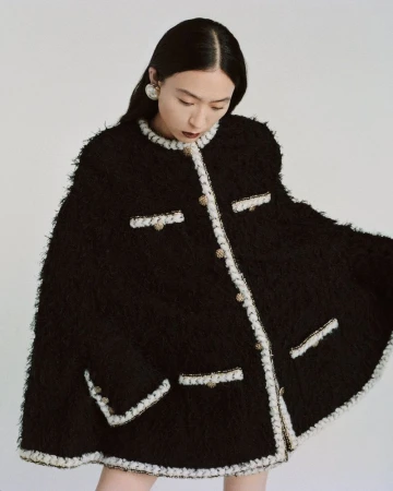 Fashionable Asian woman wearing a chic black tweed jacket with white trim, posing in a brightly lit studio against a white backdrop.