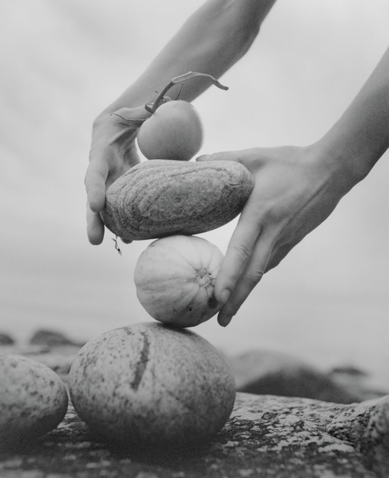 Black and white still life: hands carefully stacking round objects in outdoor setting, creating balanced and artistic composition.
