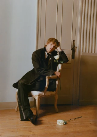Model Jordan Barrett seated in an armchair holding a white rose for Risbel Magazine editorial photography by Pepe Herreros.