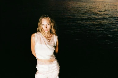 Model Bianca Szilágyi wearing white apparel against dark water for Osmos S/S 26 Campaign photographed by Zsombor Hajdu
