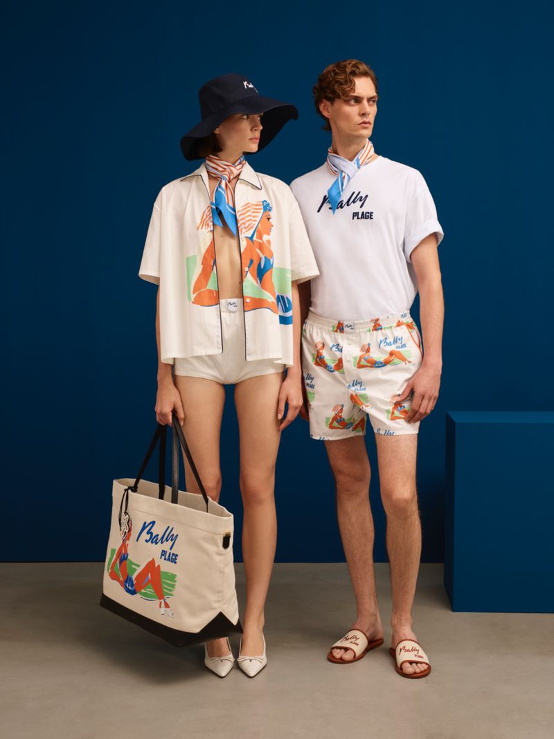Two models showcase Bally Plage apparel: a woman in an unbuttoned shirt, briefs, hat, carrying a tote; and a man in shirt, swim trunks, slides.