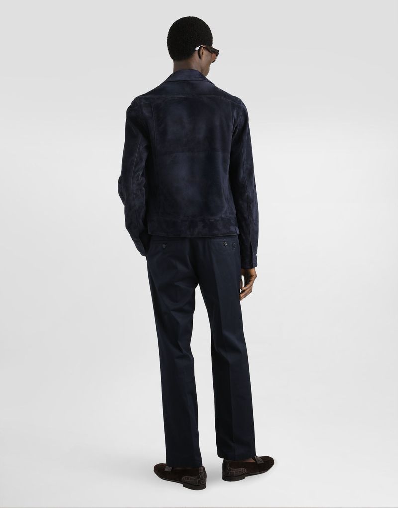 Back view of an adult male wearing a blue suede jacket and matching blue trousers, paired with dark brown loafers in a studio setting.
