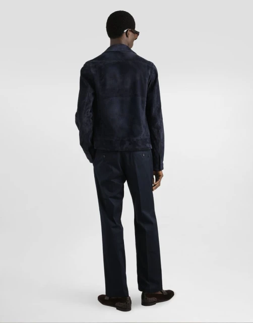 Back view of an adult male wearing a blue suede jacket and matching blue trousers, paired with dark brown loafers in a studio setting.