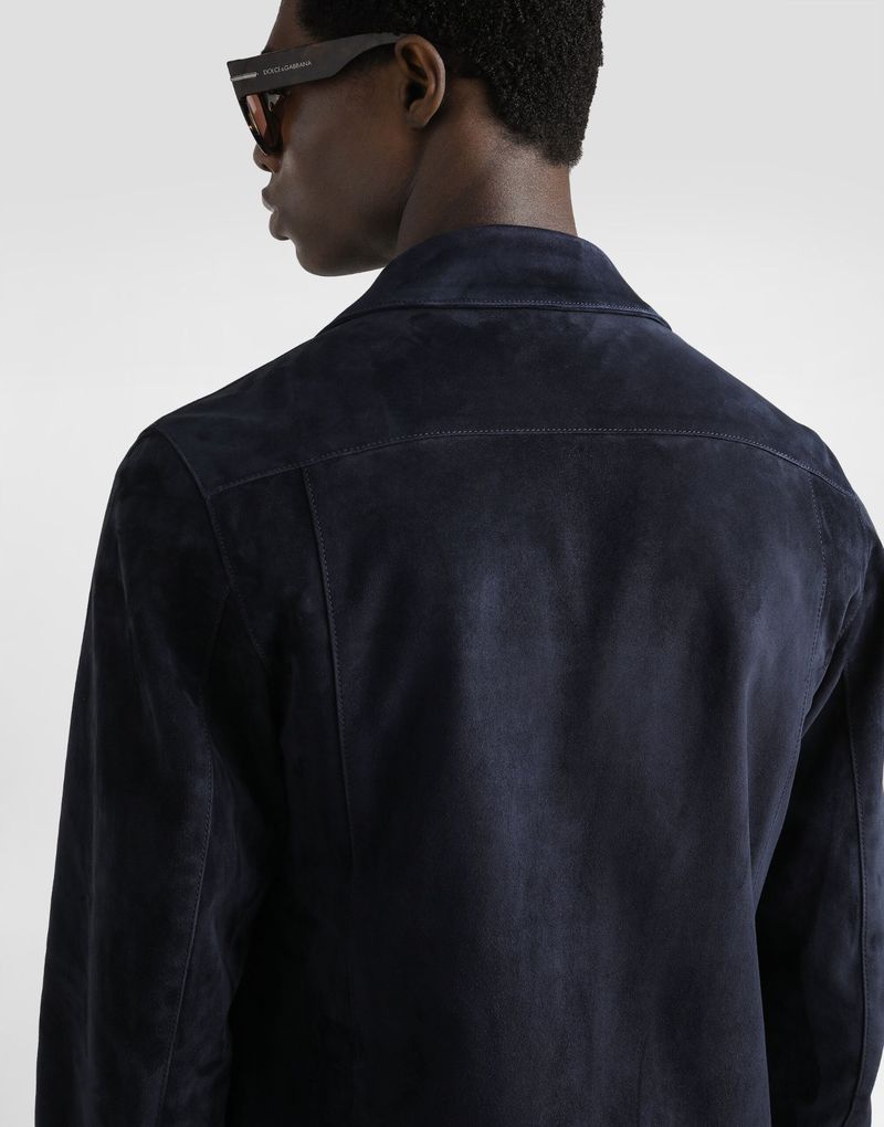 Back view of an adult man wearing a dark blue suede jacket and sunglasses. The image is shot indoors in a photo studio.