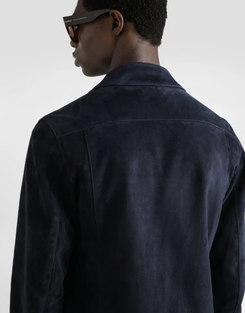 Back view of an adult man wearing a dark blue suede jacket and sunglasses. The image is shot indoors in a photo studio.