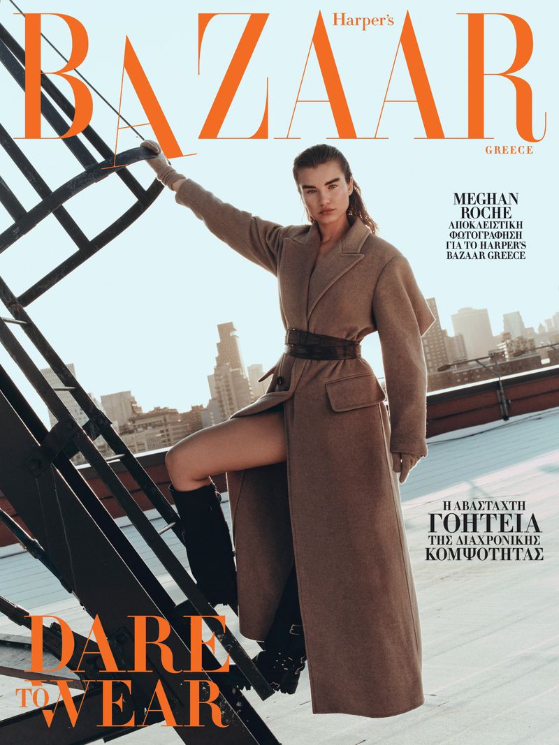 Model Meghan Roche posing on a rooftop staircase wearing a camel coat for Harper's Bazaar Greece.