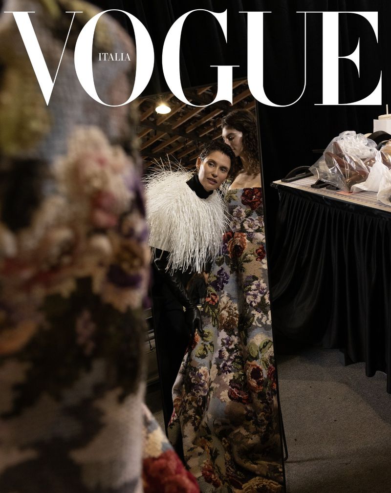 Vogue Italia cover featuring two fashion models in a backstage environment, showcasing floral-patterned gowns and a white feathered shawl.