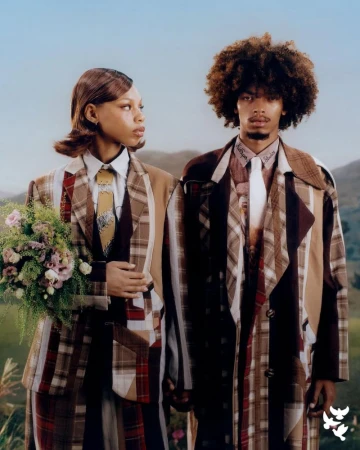 Matching couple wearing patchwork plaid suits in an outdoor setting, holding flowers, with a mountainous backdrop and soft natural light.