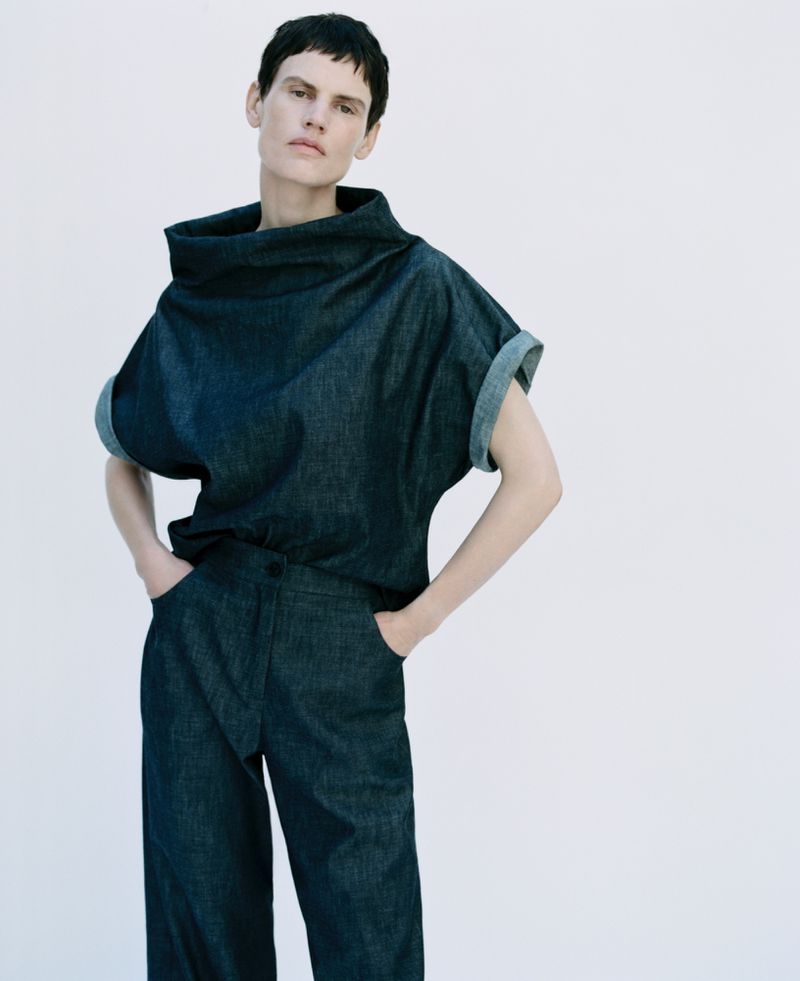 Woman posing in a denim top and pants outfit against a white backdrop, showcasing a modern, casual style.