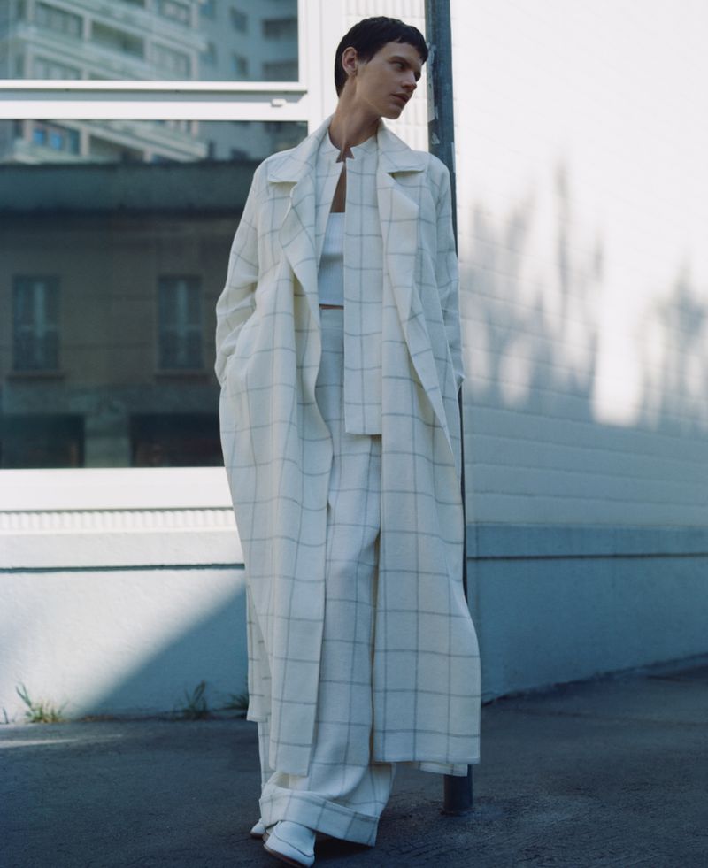 Fashionable woman in oversized plaid coat and pants walking on city street. Stylish, neutral-toned outfit with modern, confident look.